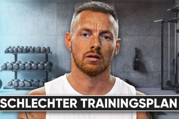 Vorschaubild des Videos "Warum ich KEINEN Ganzkörper Trainingsplan empfehle" vom Kanal CoachStef. CoachStef steht mit verschränkten Armen in einem Fitnessstudio, umgeben von Hanteln und Fitnessgeräten. Im Hintergrund ist ein Spiegel zu sehen.
